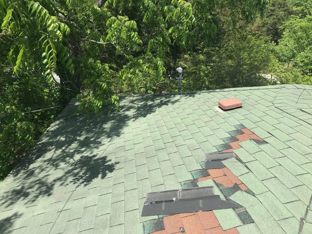 Wind damaged shingles on a house. Two layers of three tab shingles