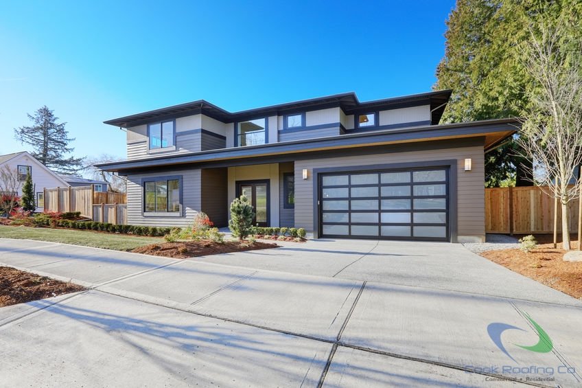 New construction home exterior with contemporary house plan  features low slope roof, brown siding and glass garage door.