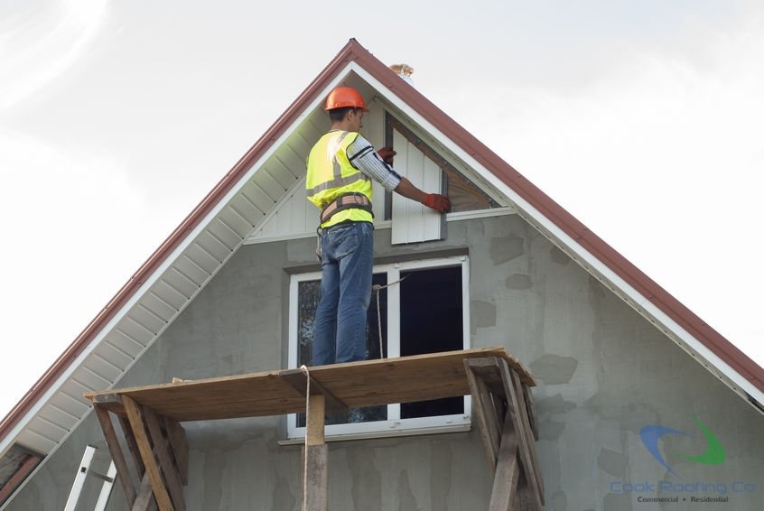 Contractor on scaffolding installing siding and soffit on the gable end and rakes of a house.