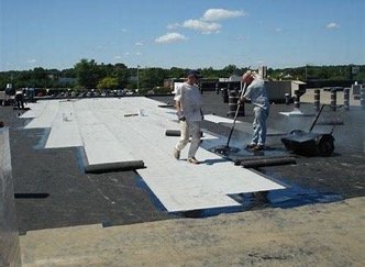 White built-up roofing being installed with rollers and roofers