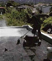 Built-up roofing being installed on a flat roof by worker with roller
