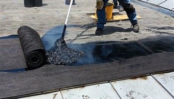 Built-up roofing being installed with a mop on a flat roof