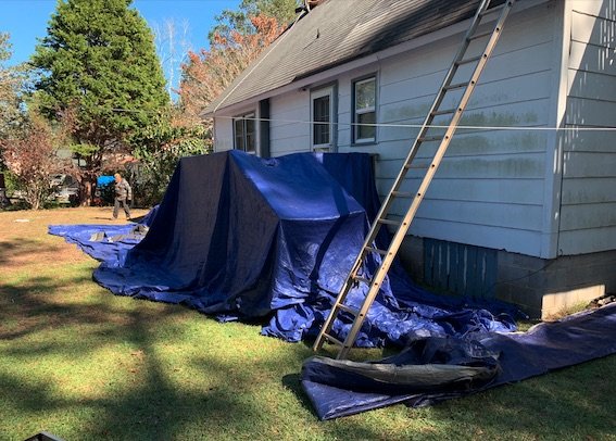 House getting roof replacement with tarping covering the rear porch and deck and landscaping