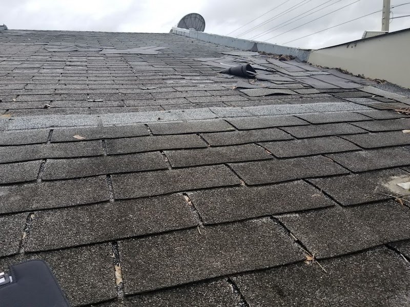 Shingles blown aside on convenience store roof with two layers of 3-tab shingles