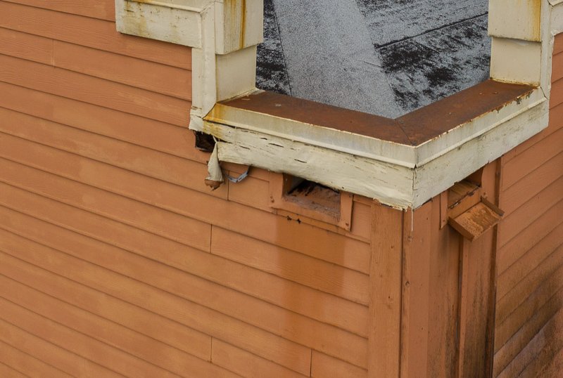 Scuppers on a restaurant roof with peeling paint and damaged trim