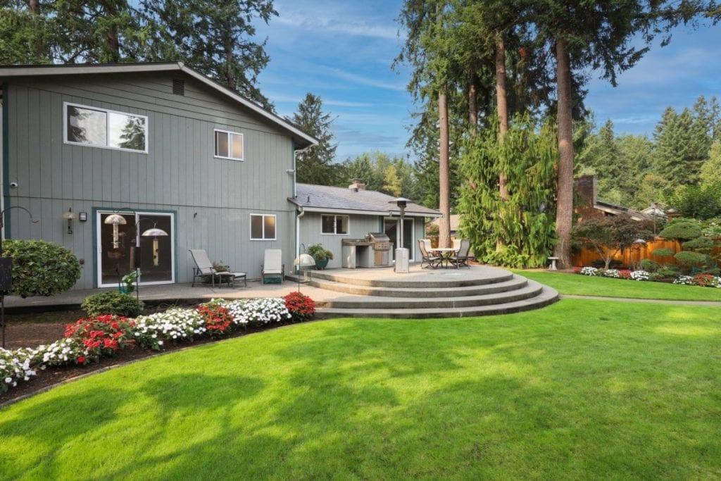 Outdoor living space, back yard with green grass, trees, patio, chairs, outdoor eating area